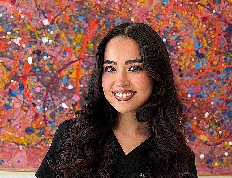 Smiling woman in front of colorful abstract painting.