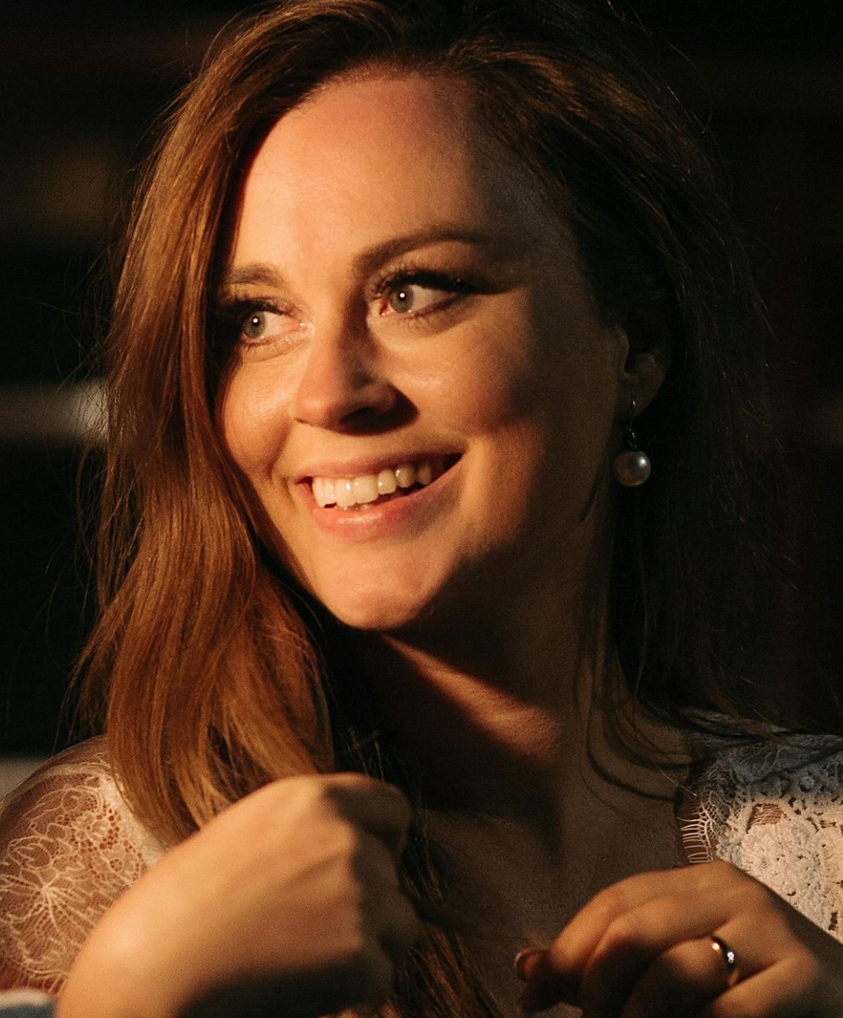 Smiling lip filler model with long hair and pearl earrings.