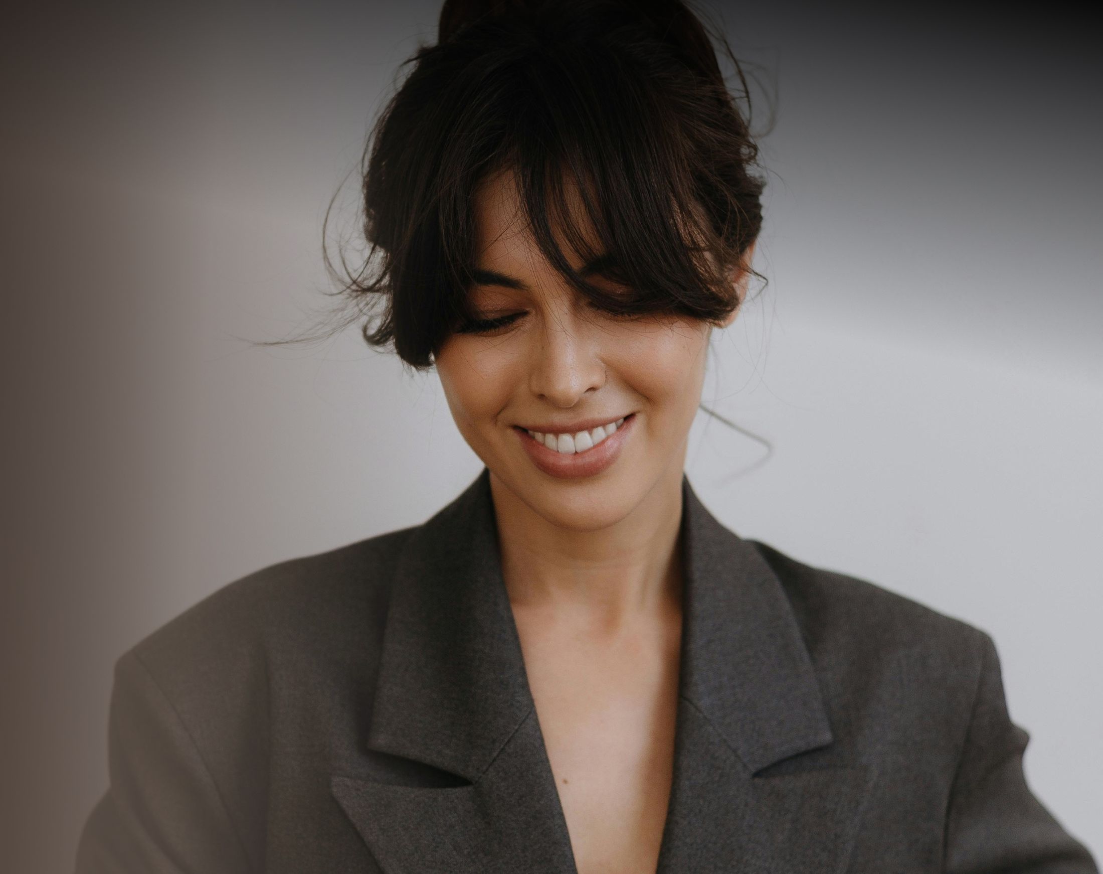 Smiling woman in a gray blazer, looking down.