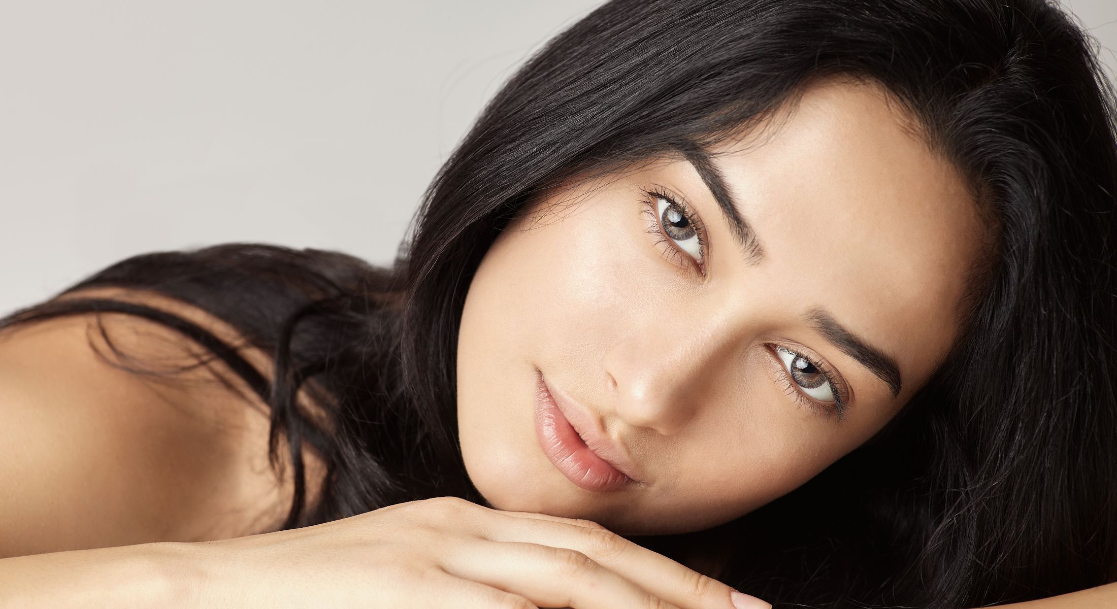 Skin rejuvenation model resting her chin on her hand, gazing.