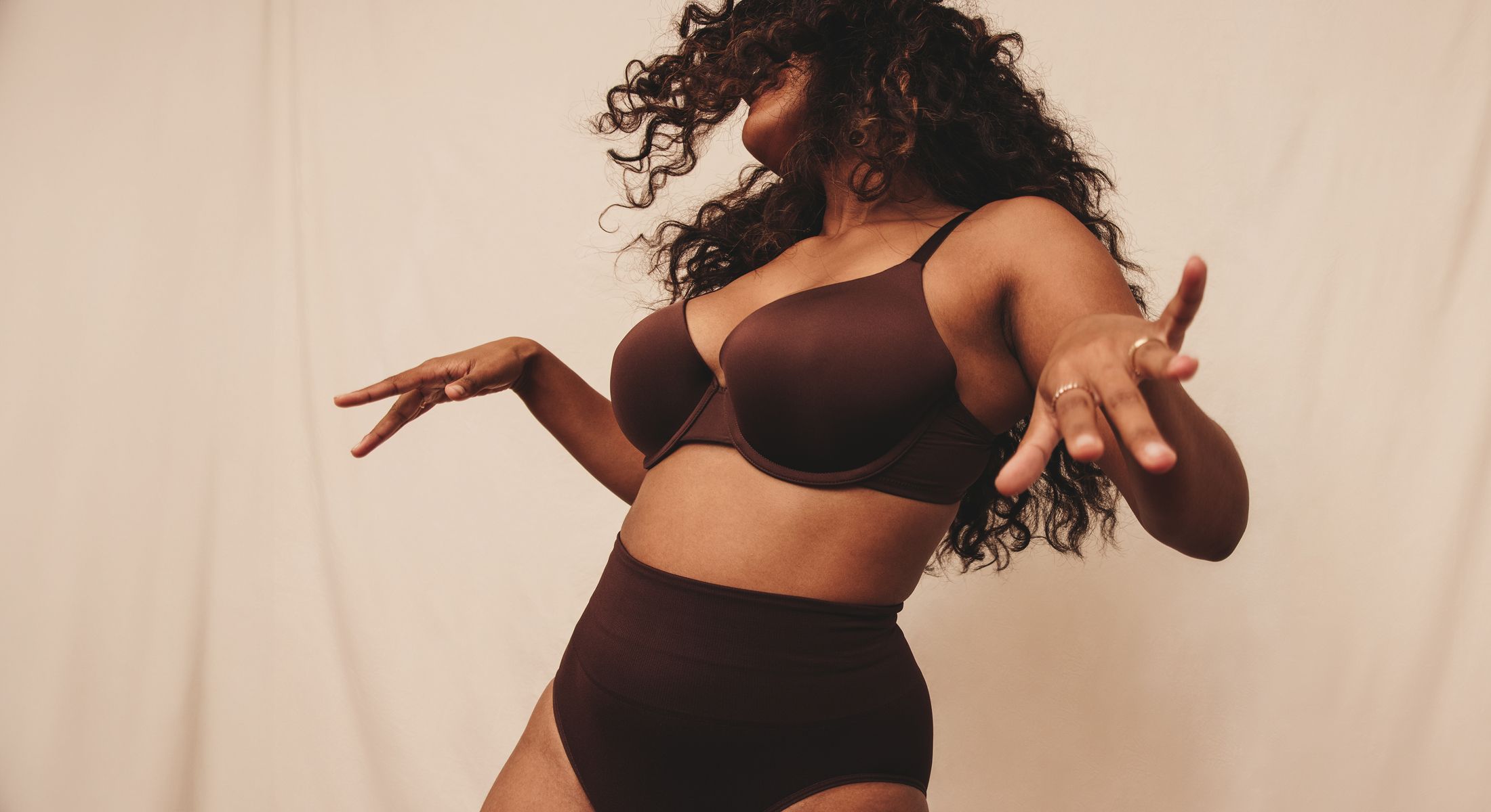 Wellness treatment model dancing, wearing dark lingerie against backdrop.