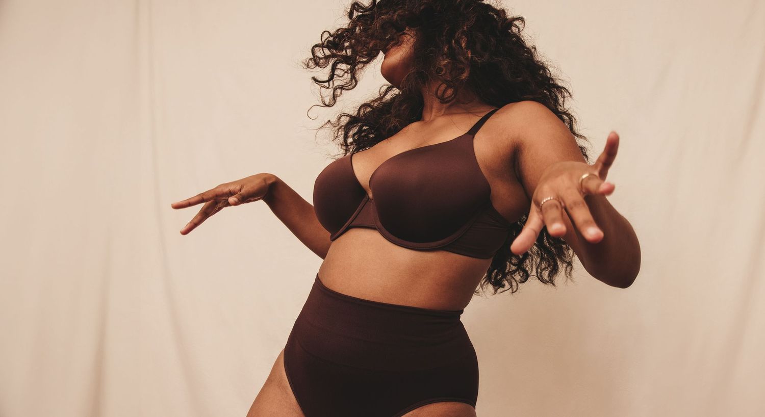 Woman in black dress posing confidently against white background.